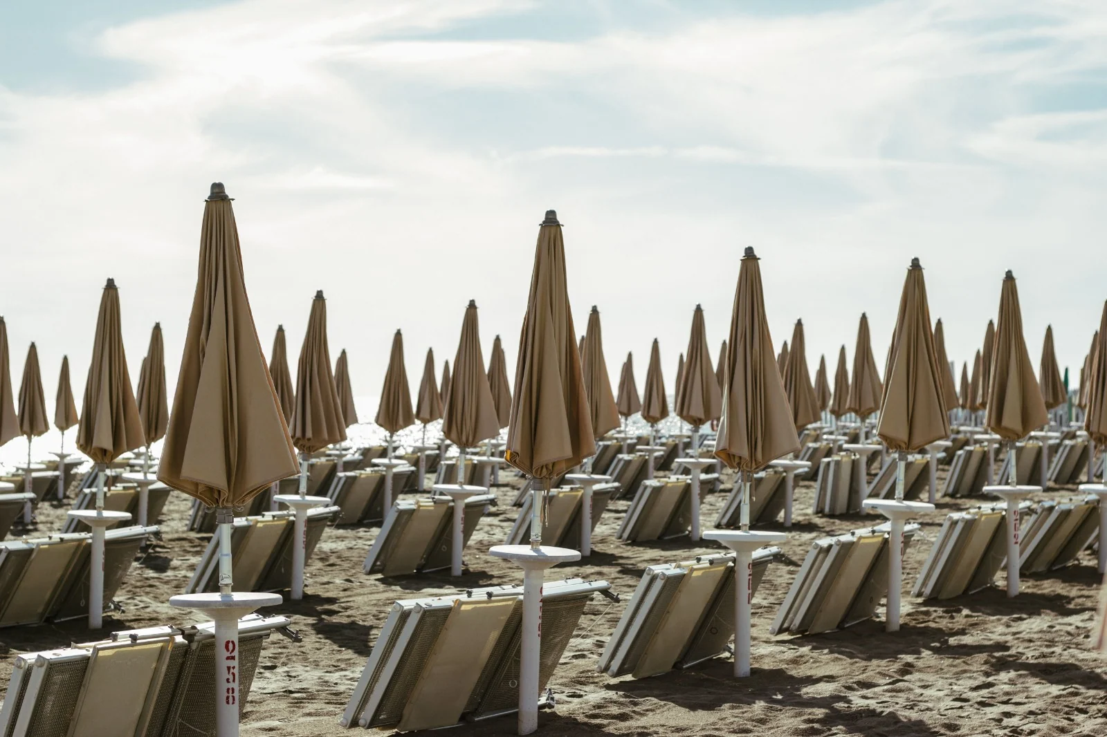Lettini e ombrelloni chiusi sulla sabbia, con il mare sullo sfondo